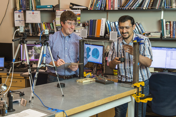 Professor and student working together with lab equipment and a computer in an engineering classroom. 