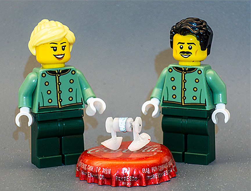 Two LEGO figures stand beside a micro walking robot as a comparison to its tiny size