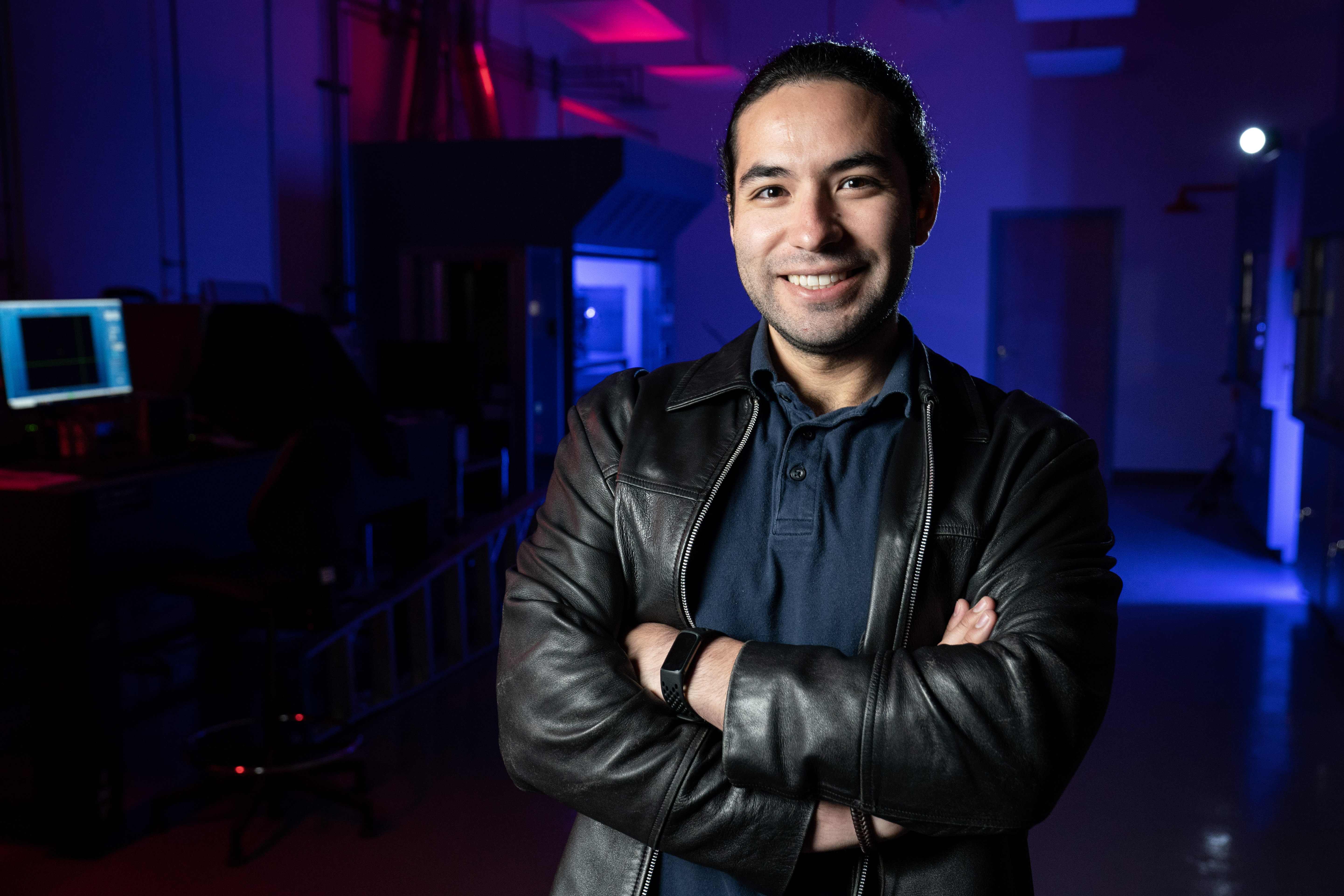 a smiling man with his arms crossed, wearing a leather jacket.