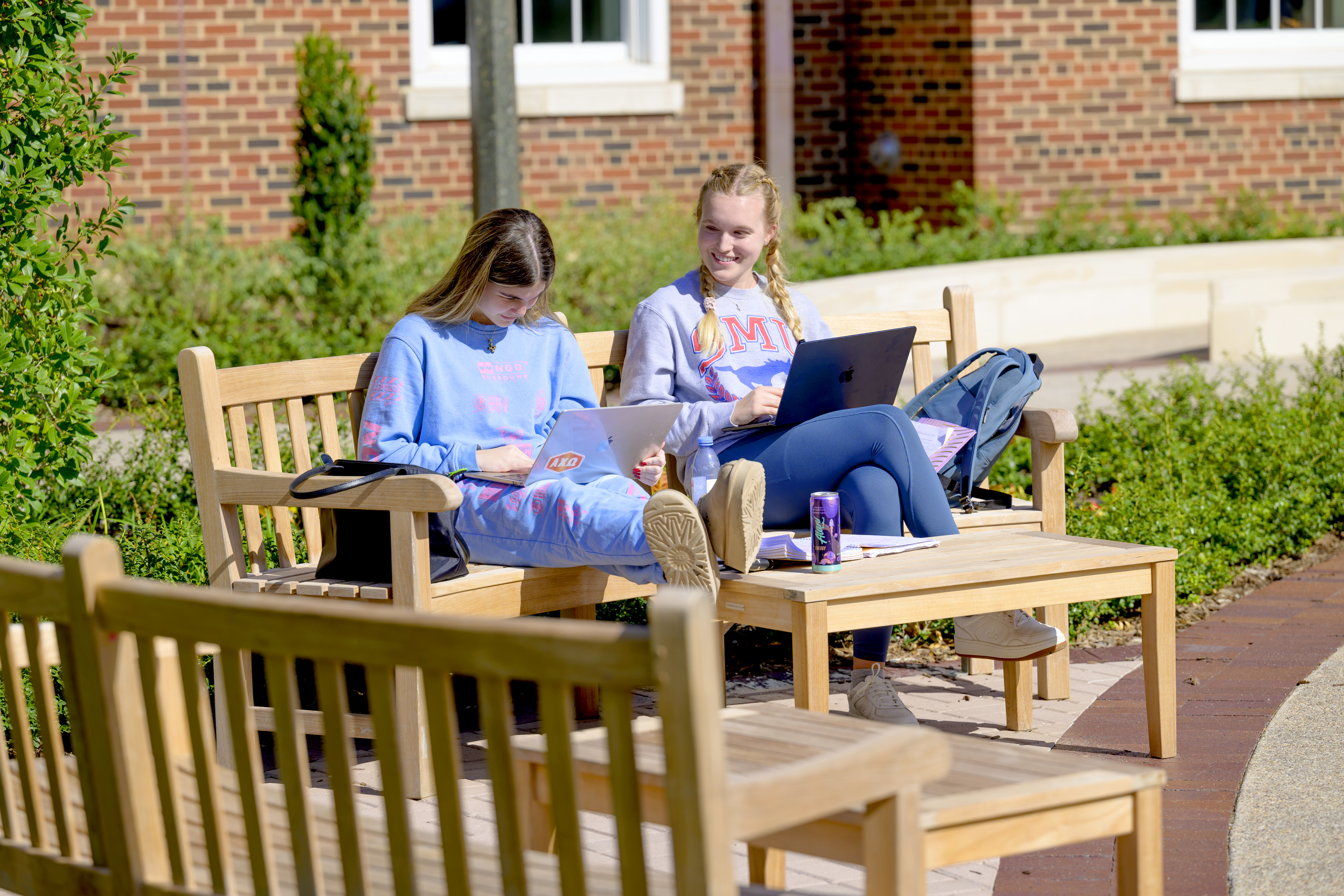 Two female students work on their laptops on a bench in the Miller courtyard