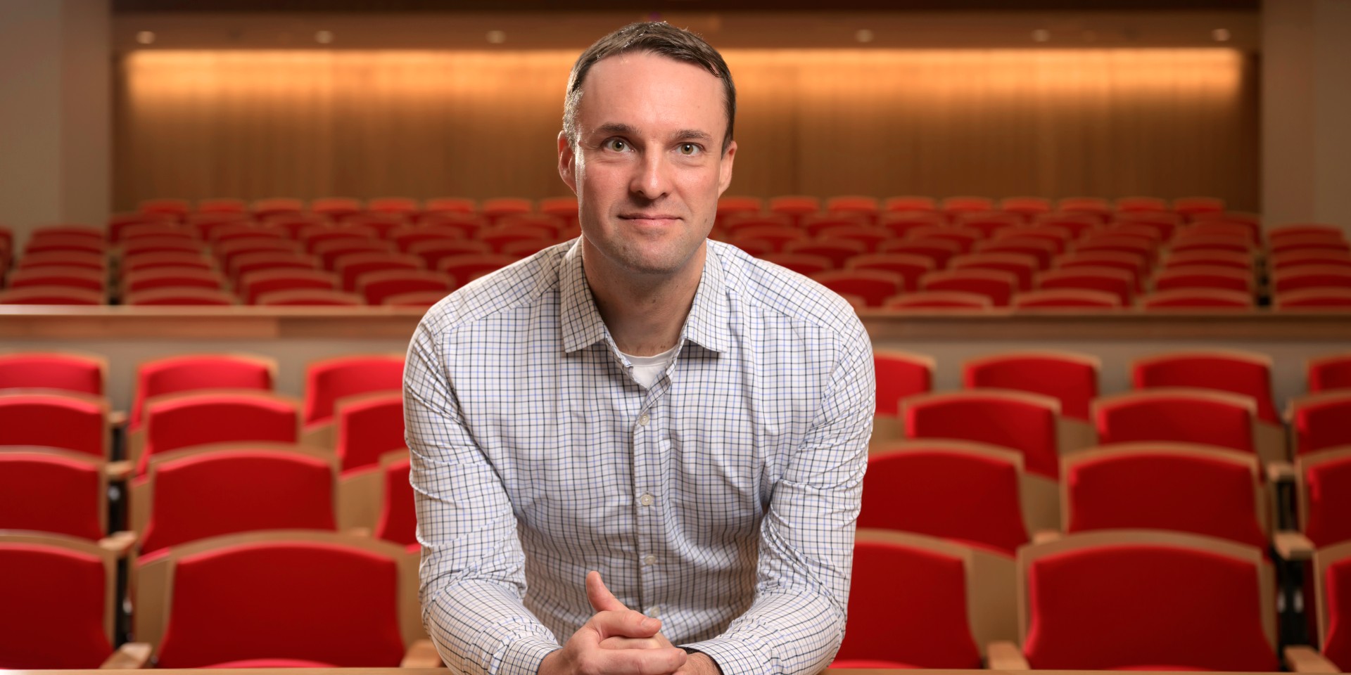 Portrait of Wayne Taylor with rows of red lecture hall seats in the background.