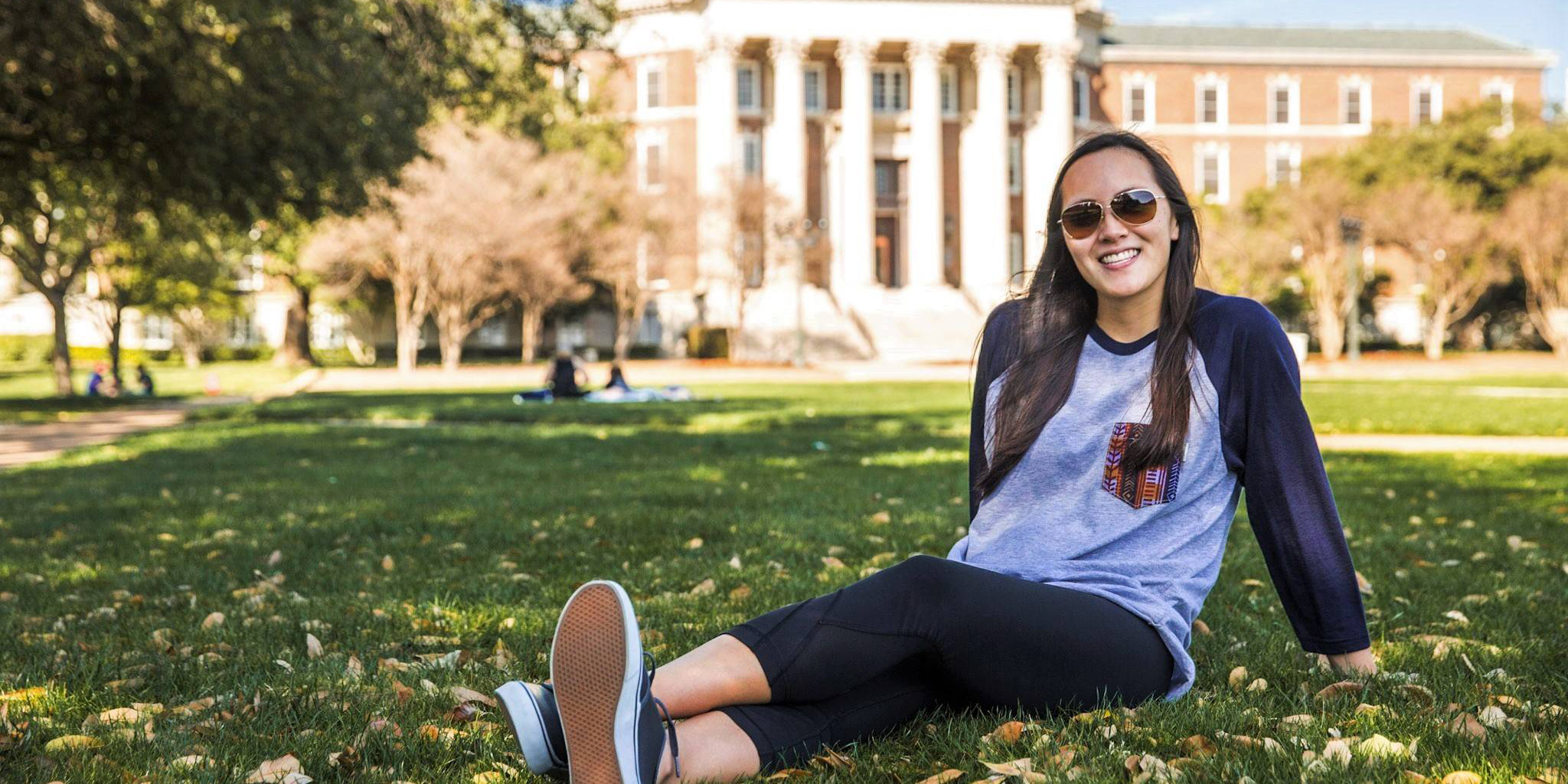 Student sitting on grass, Dallas Hall in the background.