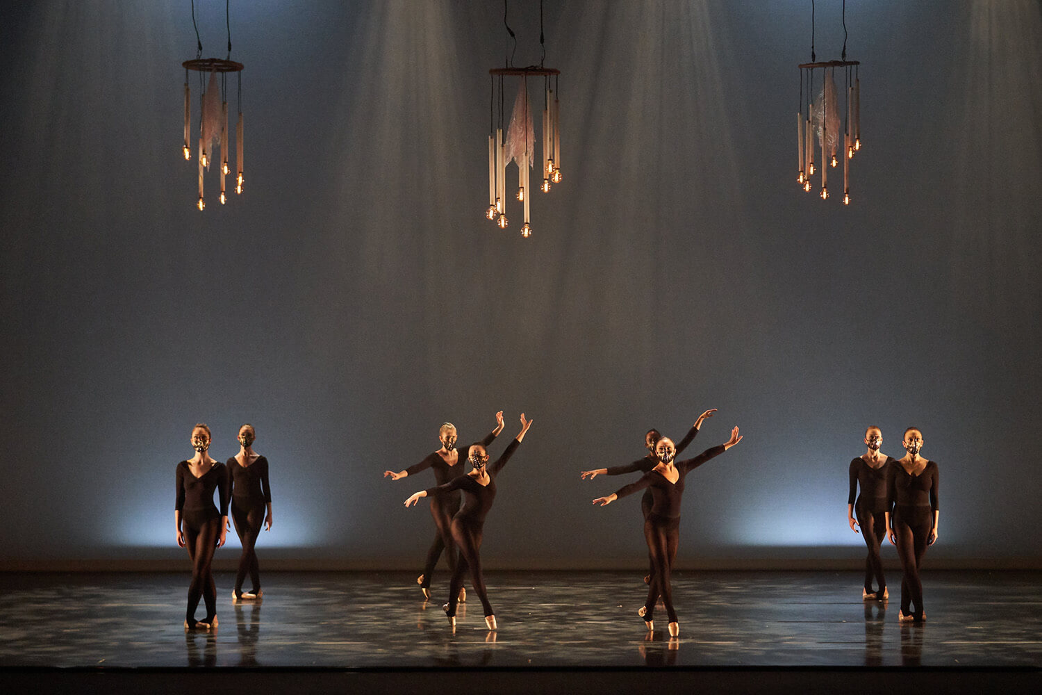 Dancers in black against a grey background wearing masks