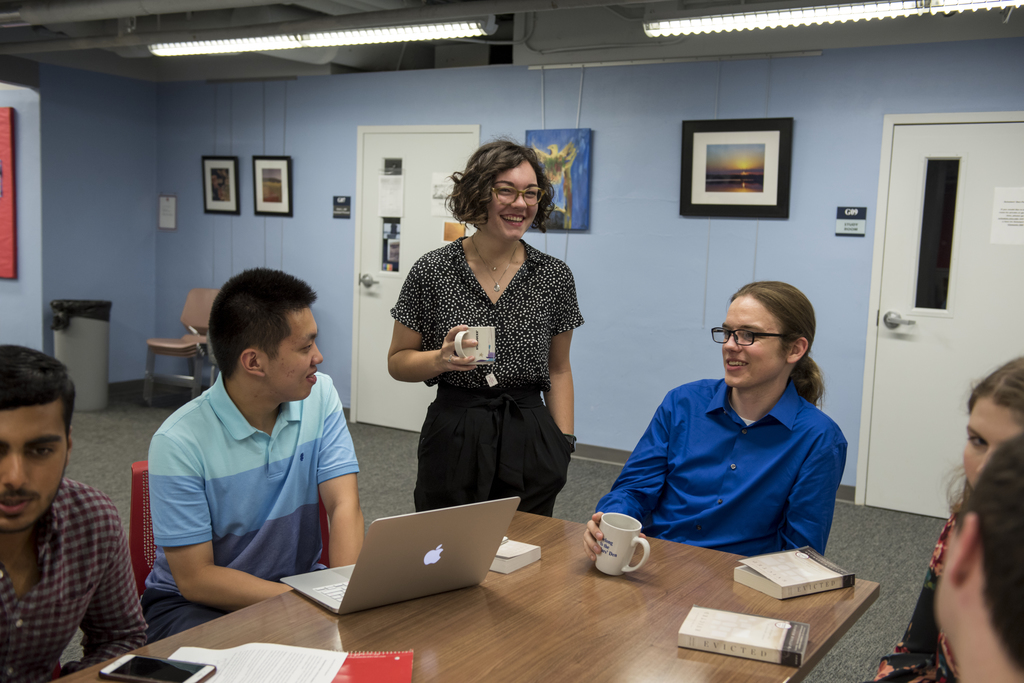 Student holding a Starbucks Nashville mug laughs, engaged in conversation with students at a table. Several students have a copy of the common reading book Evicted by Matthew Desmond, and one student has a computer open in front of him.