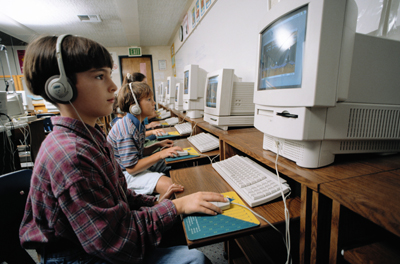 A young boy with headphoness on, participating in a reading intervention session in his first-grade classroom.
