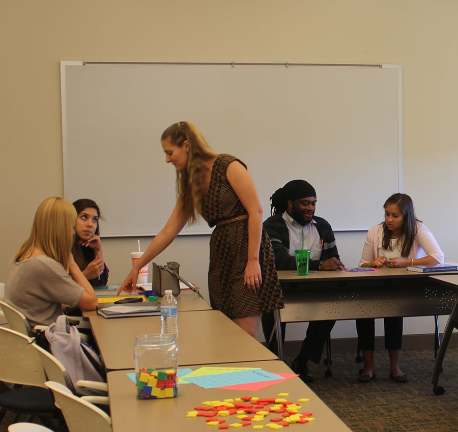 Dr. Candace Walkington stands before a table of mathematics educators, facilitating a discussion in a mathematics education classroom using manipulatives.