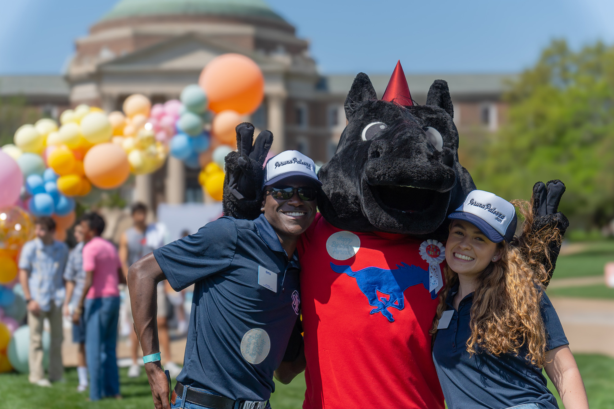 two students posing with peruna mascot outside in front of balloons and Dallas Hall