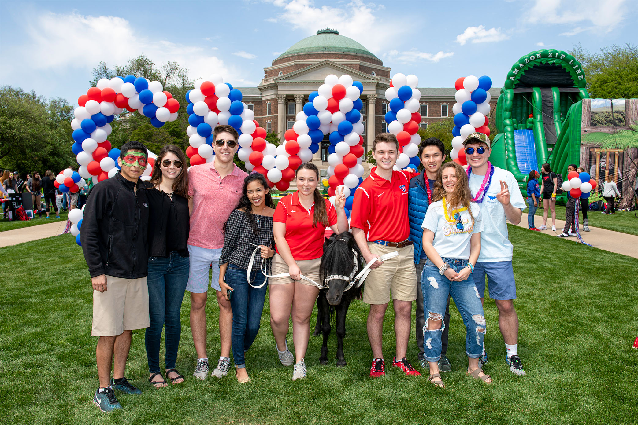 nine students on Dallas Hall Lawn with Peruna in front of 色花堂_色花堂 98堂 letter balloons in red, blue, and white