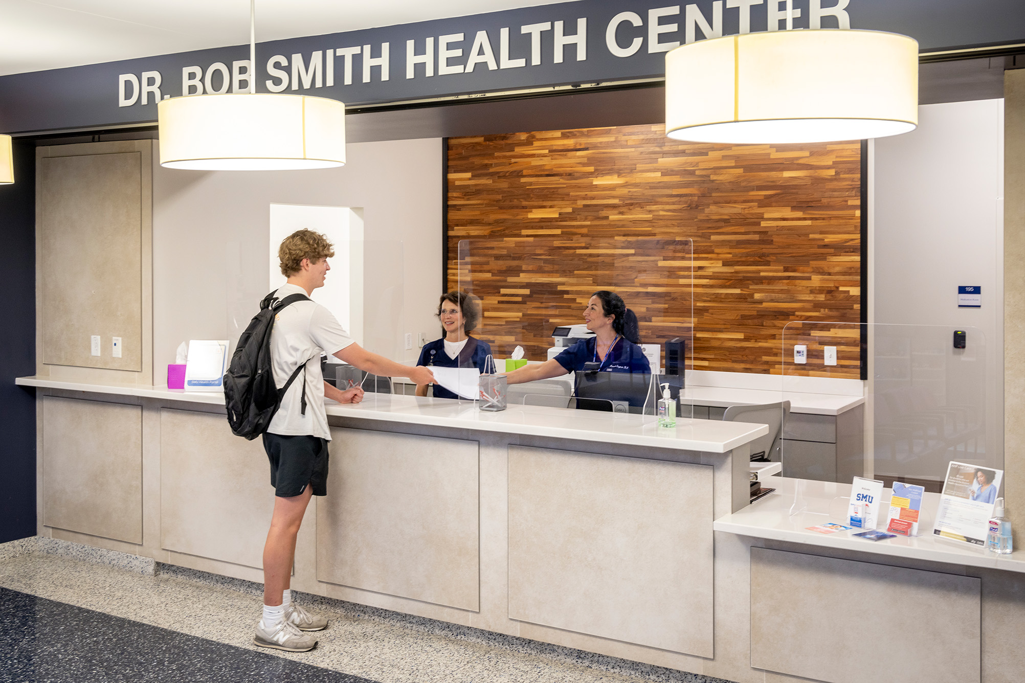 student standing at counter handing a piece of paper to two people behind the counter