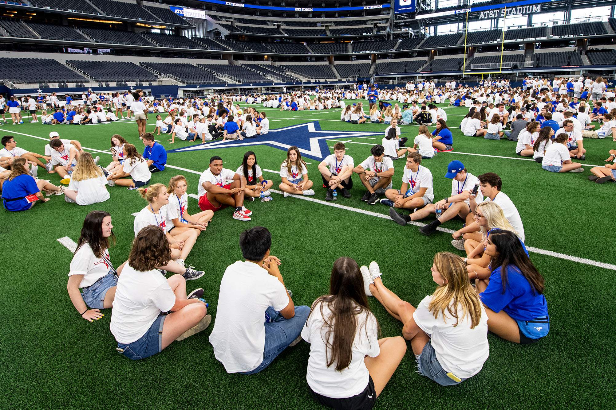 Students sitting in small group circles on the field at AT&T Stadium