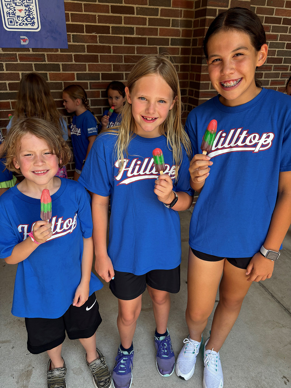 three children in blue shirts smiling with popsicles