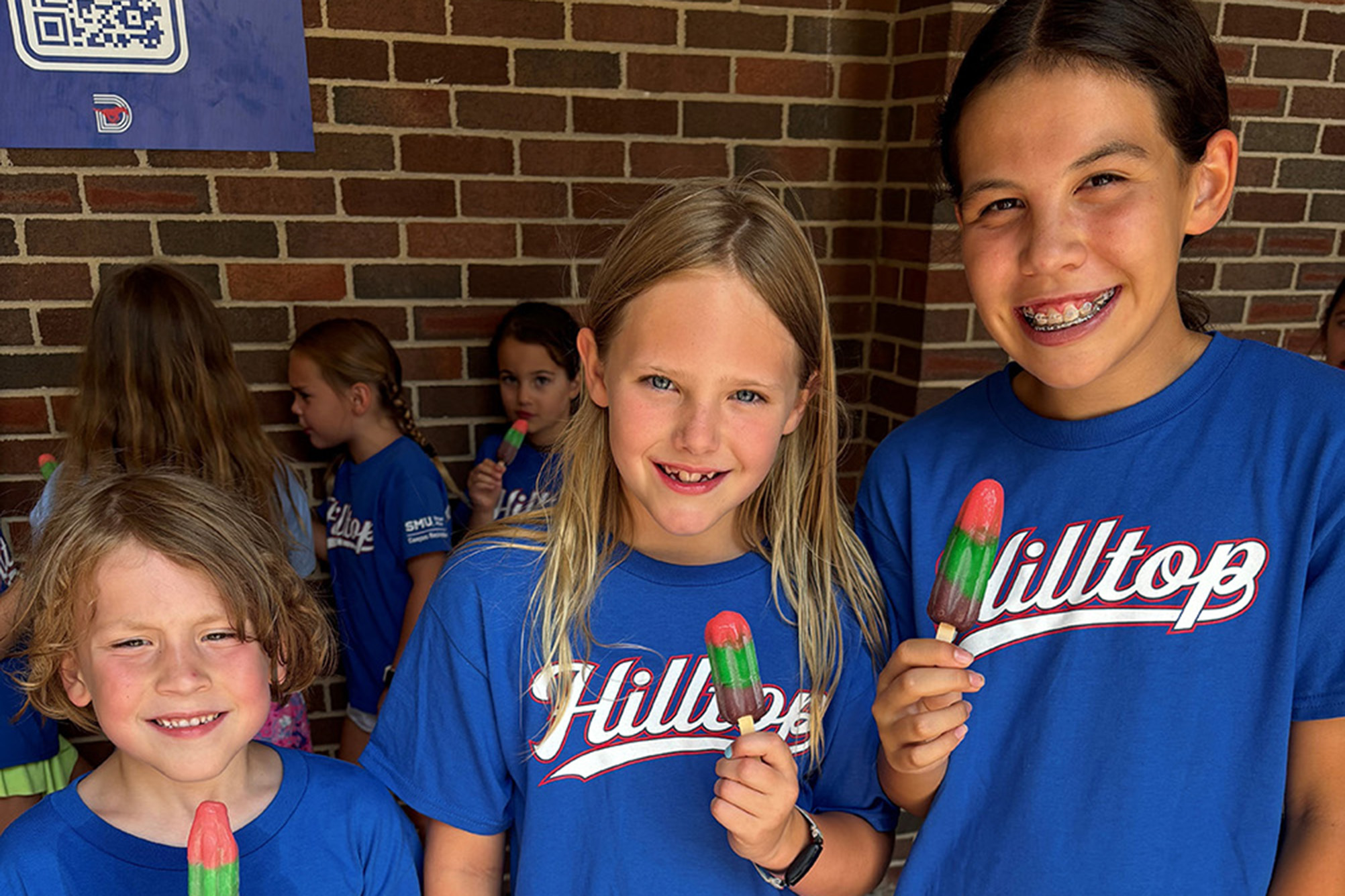 three children in blue shirts smiling with popsicles